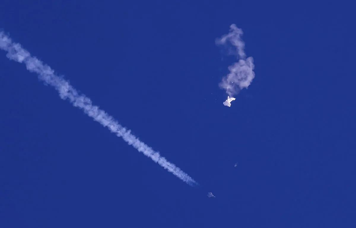 In this photo provided by Chad Fish, the remnants of a large balloon drift above the Atlantic Ocean, just off the coast of South Carolina, with a fighter jet and its contrail seen below it, on Feb. 4, 2023. (Chad Fish via AP)