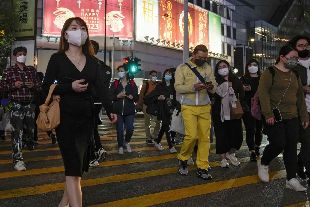 People wearing masks walk across a busy street at the Causeway Bay shopping district in Hong Kong on Feb. 7, 2023. (Andy Wong/AP Photo)