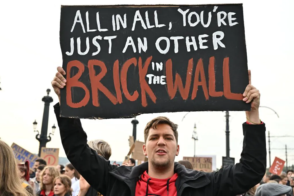 A young man holds up a placard with a quote from Pink Floyd's song "Another Brick in the Wall" as students, teachers, and sympathizers block the traffic on Margit Bridge to protest against the government's education policy in Budapest, on Oct. 5, 2022, the International Teachers' Day. (Attila Kisbenedek/AFP via Getty Images)