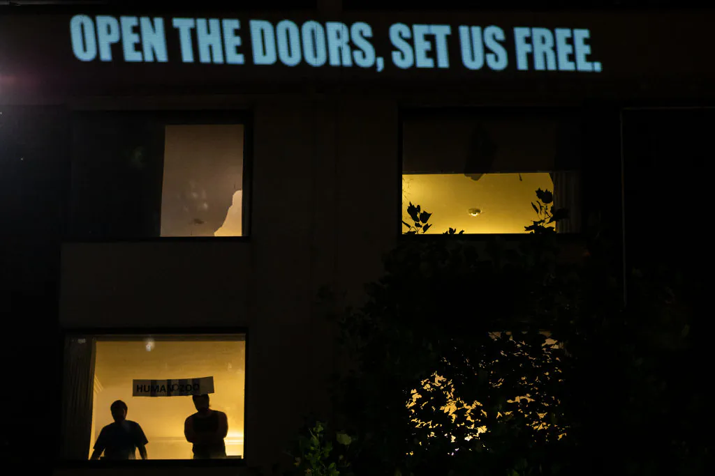 Refugees stand behind a window of the Park Hotel in Carlton as supporters project messages on the wall in Melbourne, Australia, on Jan. 8, 2022. (Diego Fedele/Getty Images)