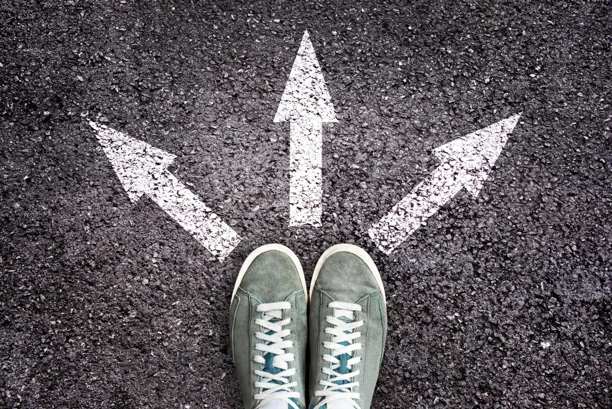 Shoes and arrows pointing in different directions on asphalt floor; school choice, education. (Delpixel/Shutterstock)