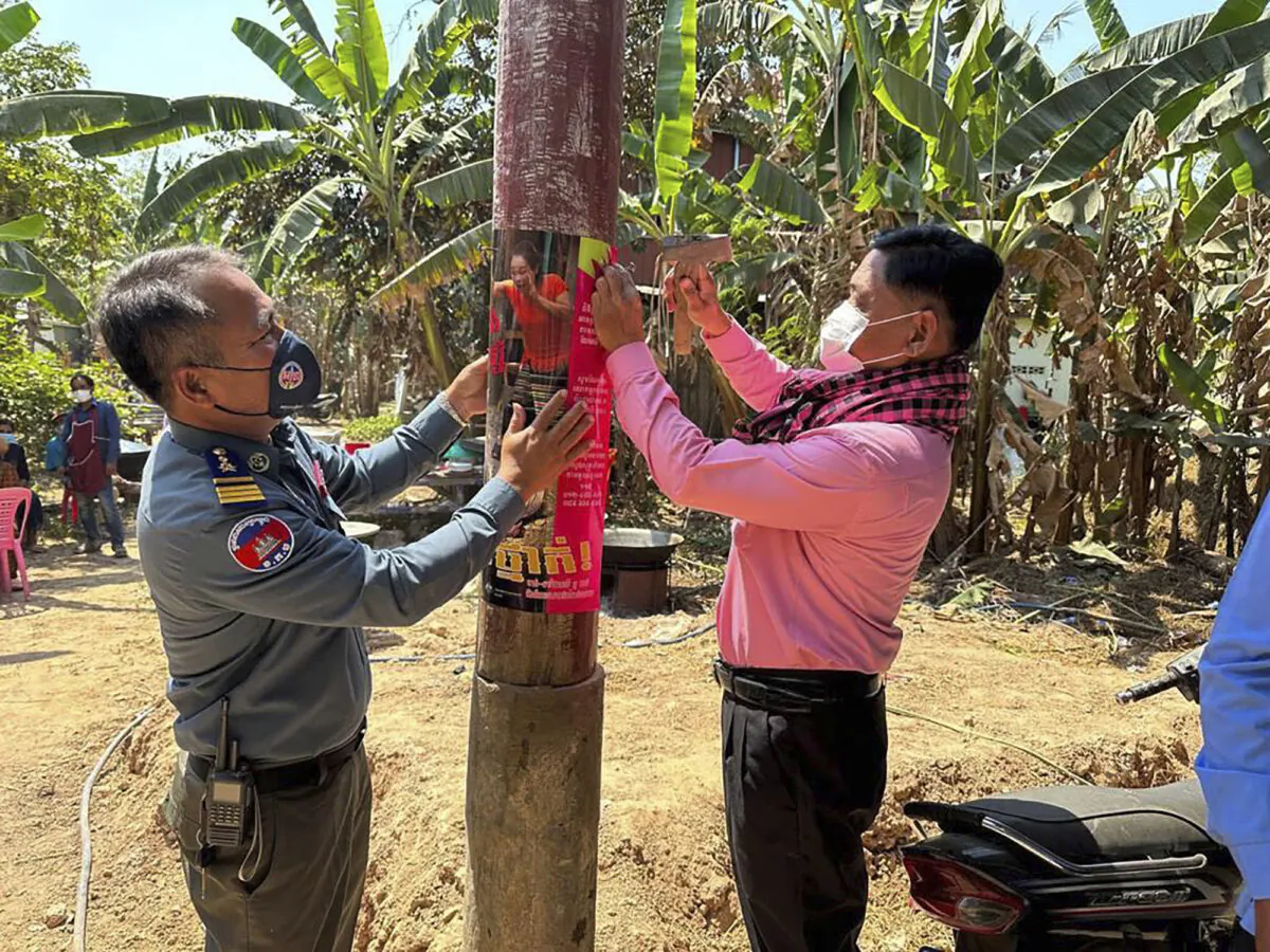A Cambodia animal health officer (R) and a military police officer place posters about awareness of H5N1 virus threats in hopes of educating villagers to take care of their health in Prey Veng eastern province, Cambodia, on Feb. 23, 2023. (Cambodia Ministry of Health via AP)