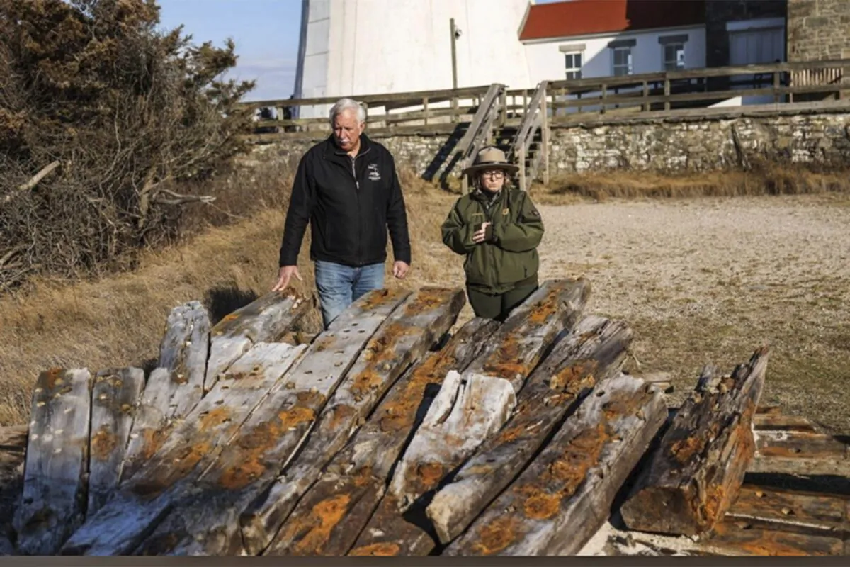 Tony Femminella, executive director of the Fire Island Lighthouse Preservation Society, and Betsy DeMaria, museum technician with Fire Island National Seashore, stand beside a section of the hull of a ship believed to be the SS Savannah, at the Fire Island lighthouse in New York on Jan. 27, 2023. (Steve Pfost/Newsday via AP)