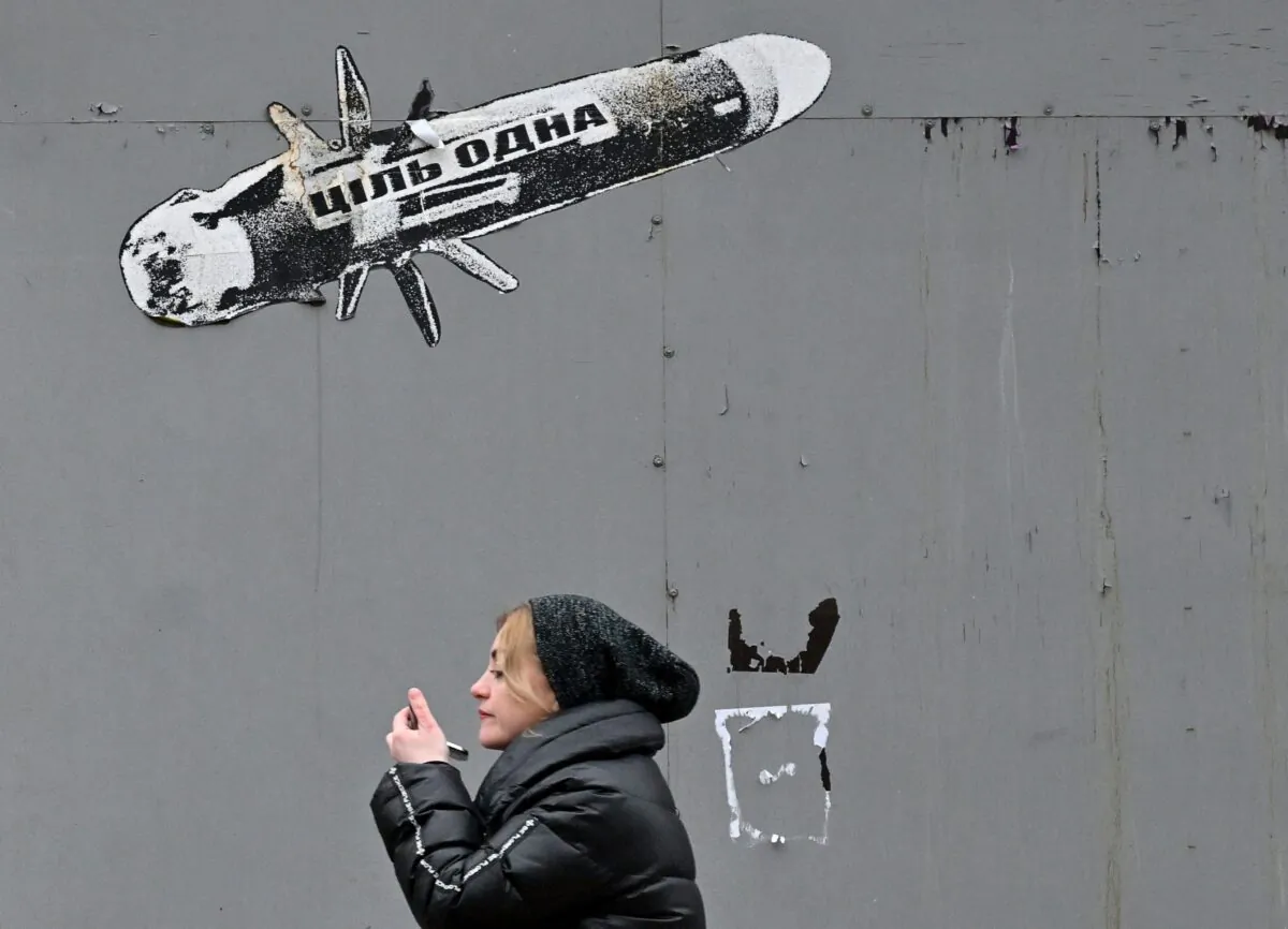 A woman looks at a smartphone in front of graffiti depicting an anti-tank missile reading "The only target," in Kyiv, Ukraine, on Jan. 25, 2023. (Sergei Supinsky/AFP via Getty Images)