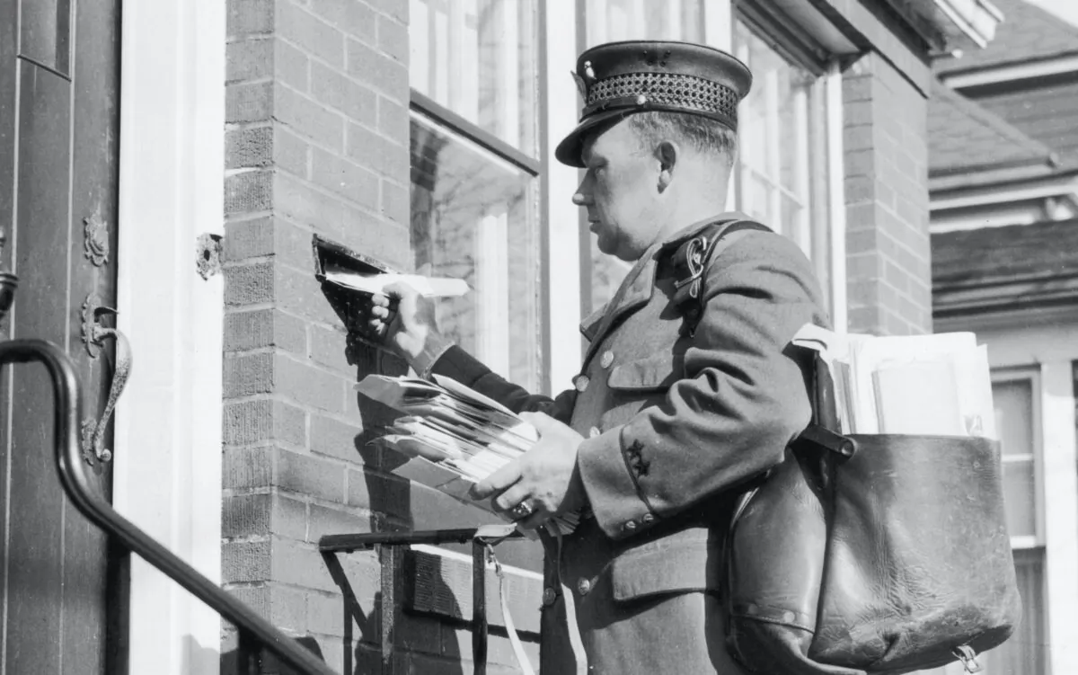 A postman slips a letter through a slot in the wall of a house in 1959 in a file photo. (FPG/Getty Images)