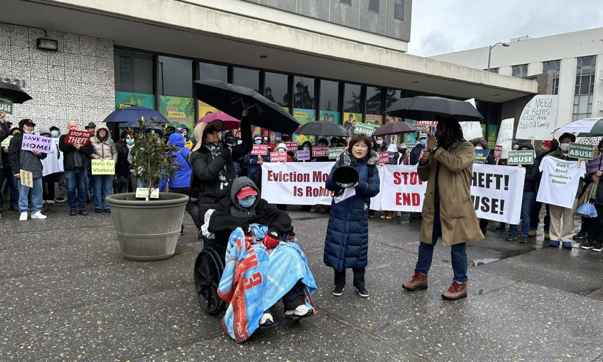 Dozens of people hold up signs protesting against an eviction moratorium while a property owner sitting in a wheelchair continues his hunger strike in Oakland, Calif., on Feb. 26, 2023. (Xue Mingzhu/The Epoch Times)