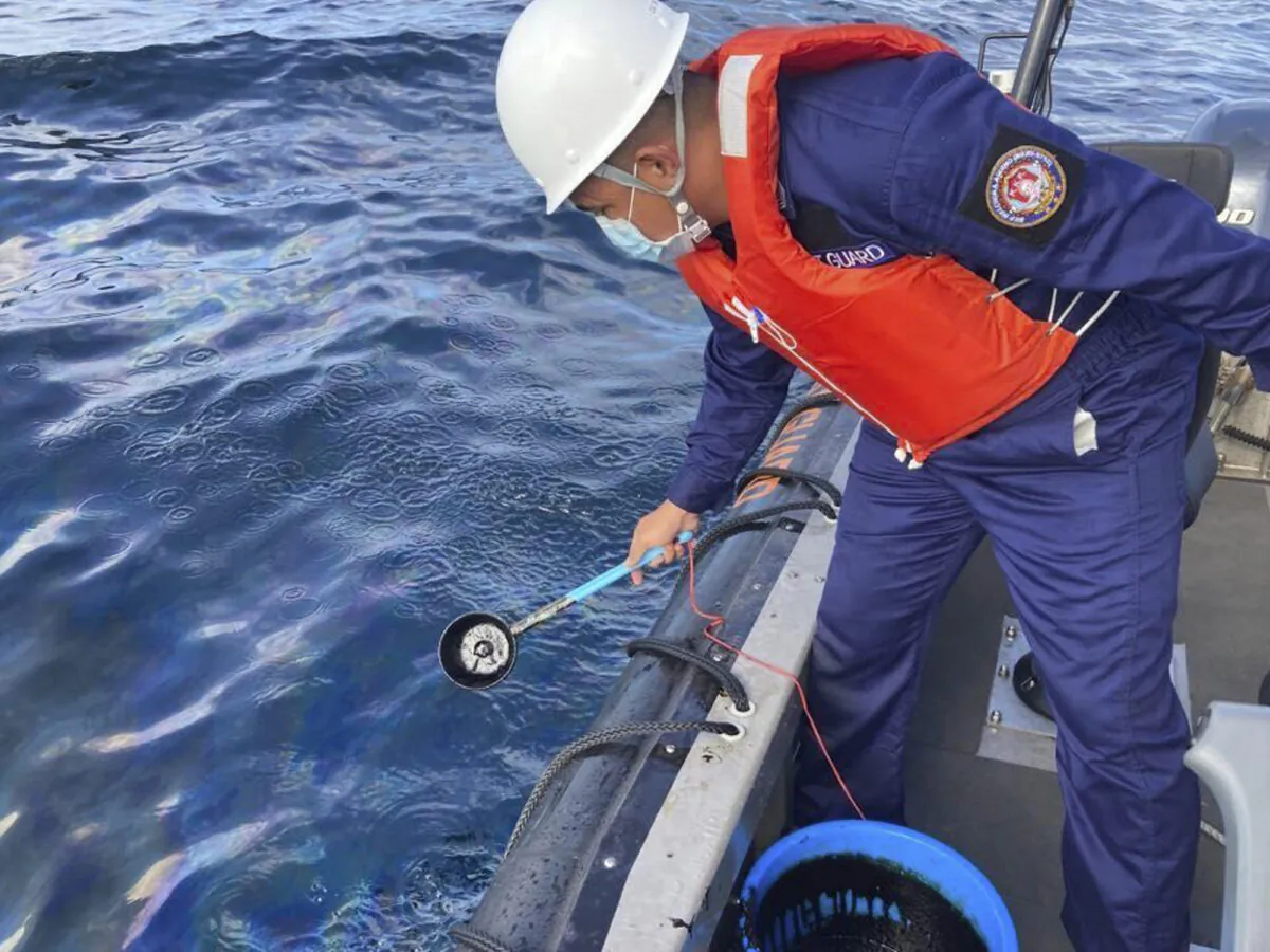 A coast guard personnel collects water samples from an oil spill in the waters off Naujan, Oriental Mindoro, central Philippines, on March 2, 2023. (Philippine Coast Guard via AP)