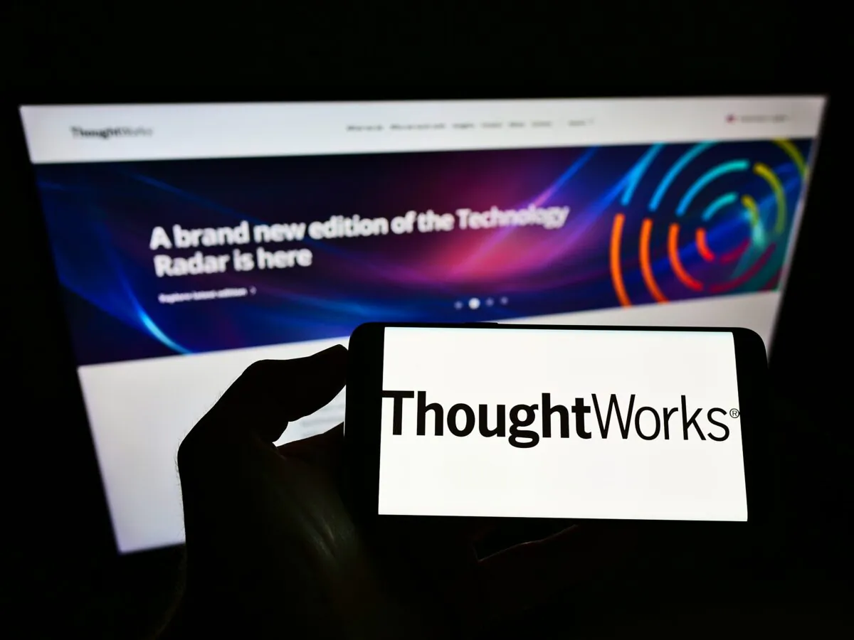 A person holds a smartphone with the logo of U.S. software company ThoughtWorks Inc. on screen in front of its website. (T. Schneider/Shutterstock)