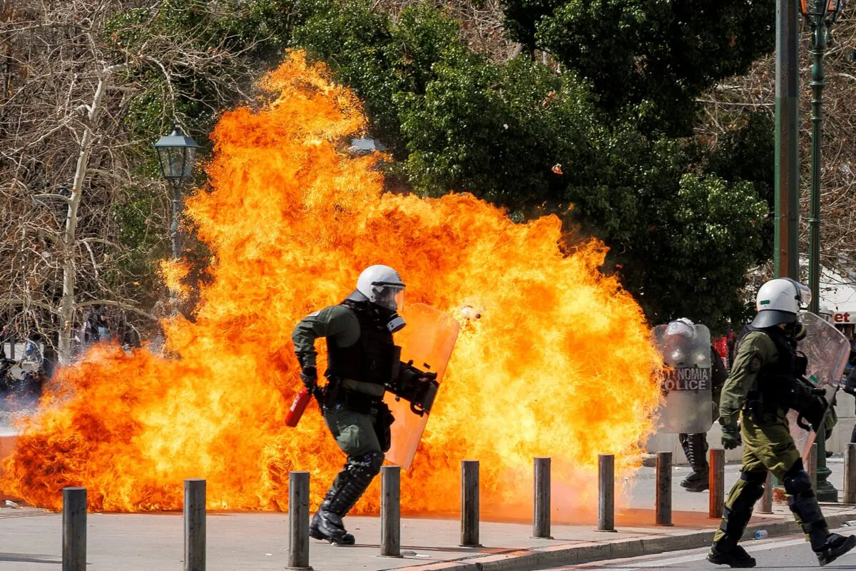 A riot police officer walks next to flames as clashes take place during a demonstration following the collision of two trains, near the city of Larissa, in Athens, Greece, on March 5, 2023. (Alkis Konstantinidis/Reuters)