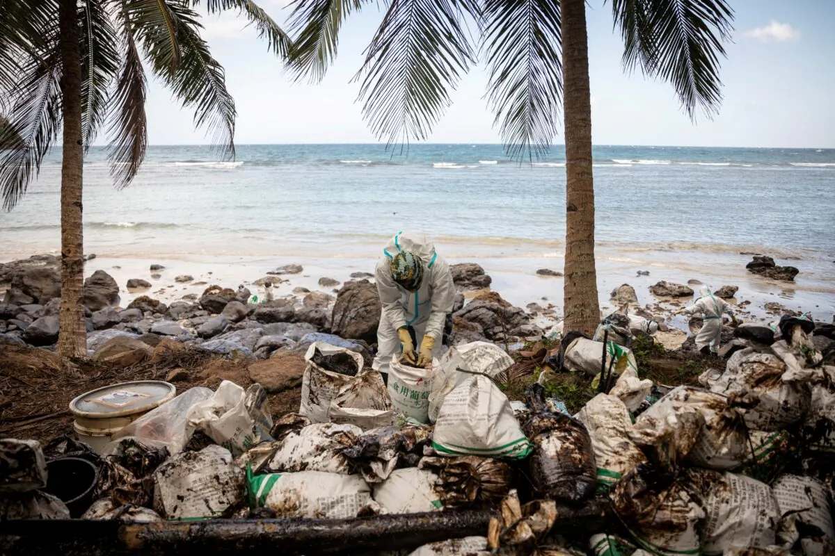A volunteer dressed in personal protective equipment gathers the oil spill collected from the sunken fuel tanker MT Princess Empress, on the shore of Pola, in Oriental Mindoro Province, Philippines, on March 7, 2023. (Eloisa Lopez/Reuters)