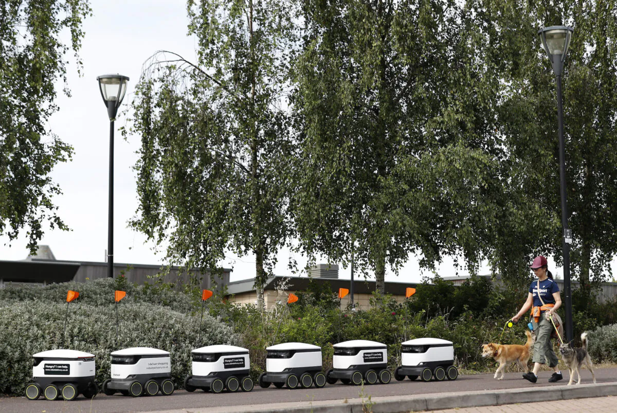 A woman walks her dogs past Starship delivery robots waiting for orders in Milton Keynes, England, on July 23, 2020. (Darren Staples/Getty Images)