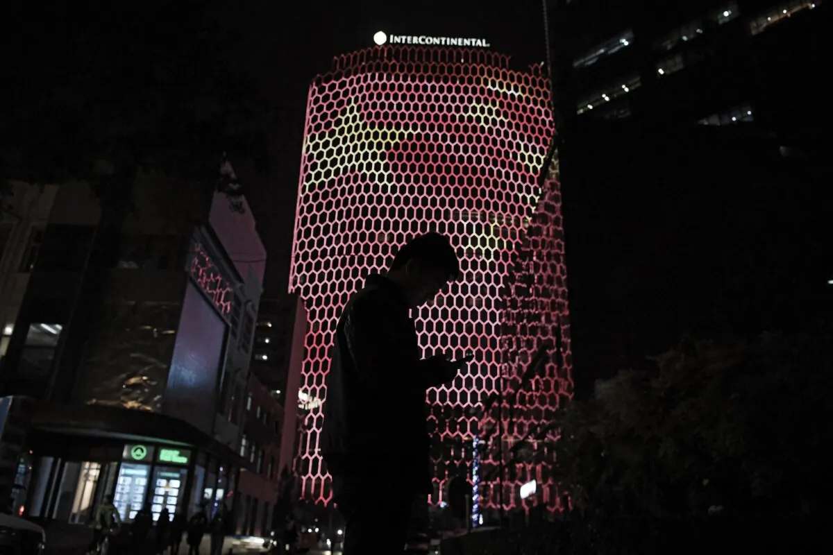 A man looks at his phone near a giant image of the Chinese national flag on the side of a building in Beijing, during the ongoing 19th Communist Party Congress on Oct. 23, 2017. (Greg Baker/AFP via Getty Images)