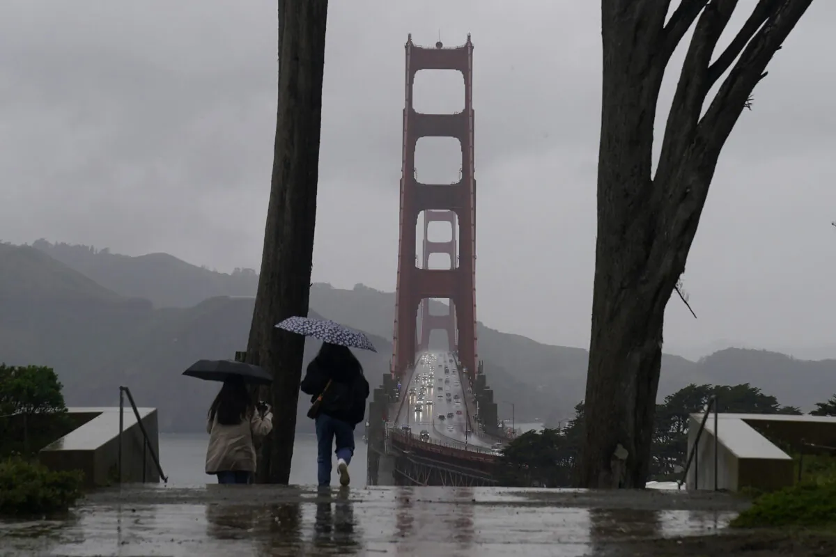 Traffic moves on the Golden Gate Bridge as people carry umbrellas while walking down a path at the Golden Gate Overlook in San Francisco on March 9, 2023. (Jeff Chiu/AP Photo)