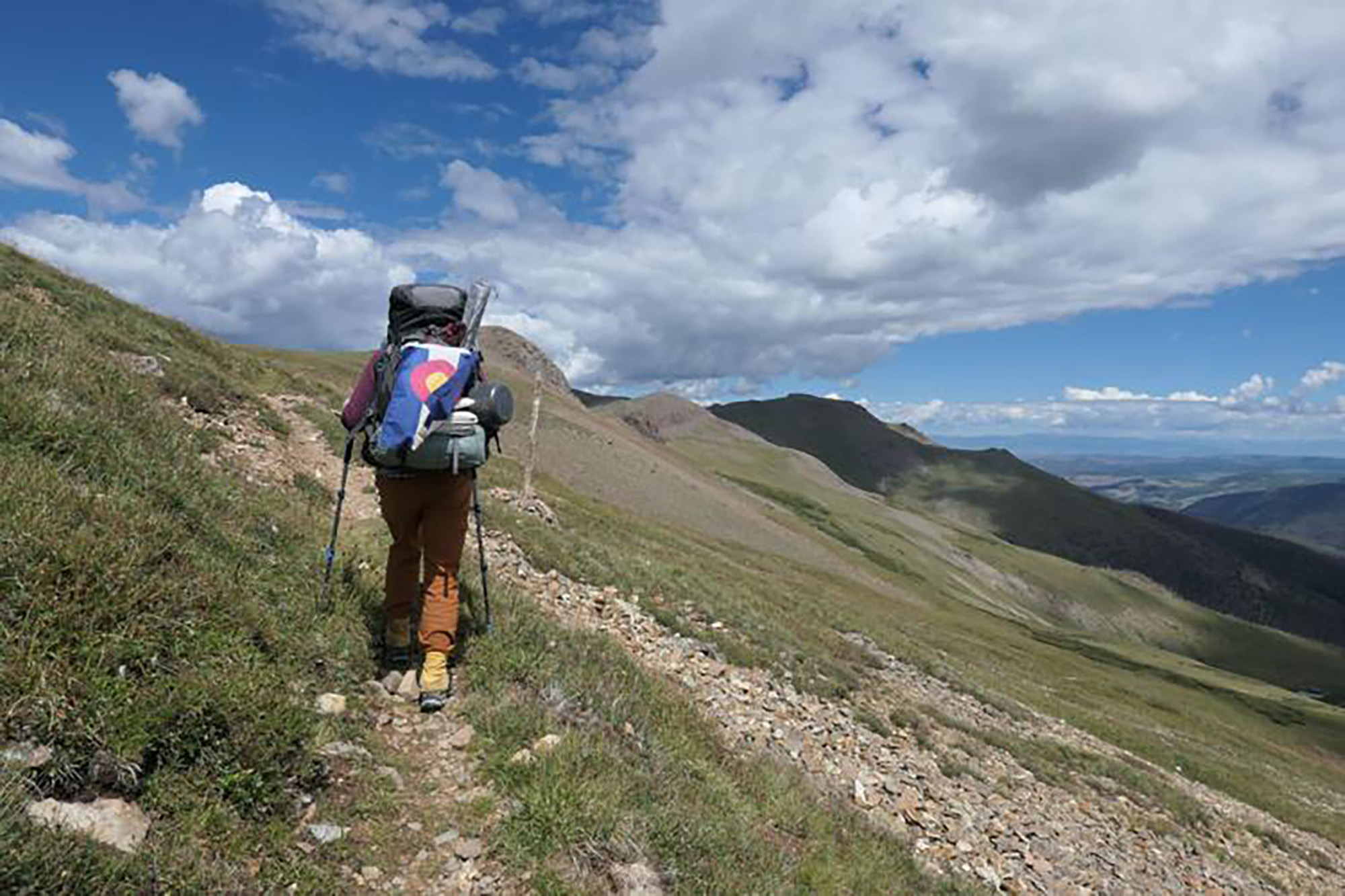 India Wood walked with a Colorado flag as she made her way across the state to its corners. Her she is on a trail in the San Juan Mountains. 