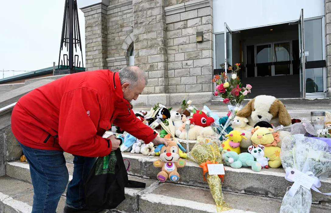 Church volunteer Daniel Theriault places a plush toy on the steps of a church in Amqui, Que., on March 14, 2023. Two people were killed and nine others were injured the previous afternoon when a pickup truck plowed into pedestrians who were walking beside a road in the eastern Quebec town of Amqui. (Jacques Boissinot/The Canadian Press)