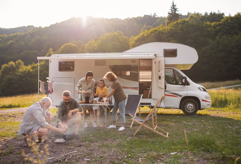Multi-generation,Family,Sitting,And,Eating,Outdoors,By,Car,,Caravan,Holiday