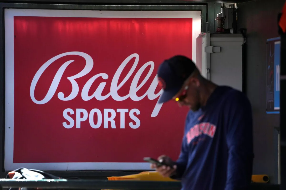 A member of the Houston Astros stands in the dugout in front of a Bally Sports sign before the team's spring training baseball game against the St. Louis Cardinals in Jupiter, Fla., on March 2, 2023. (Jeff Roberson/AP Photo)