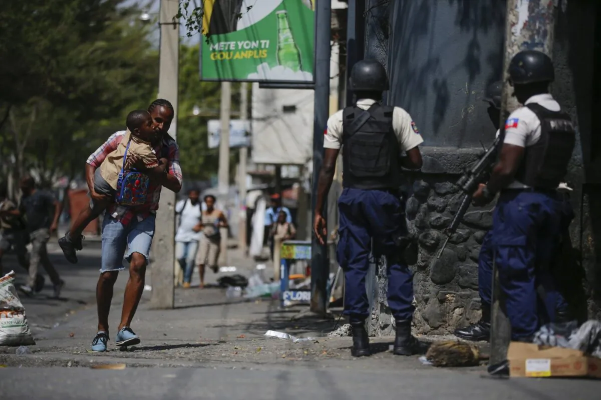 A parent, carrying his child after picking him up from school, runs past police as they carry out an operation against gangs in the Bel-Air area of Port-au-Prince, Haiti, on March 3, 2023. (The Associated Press/Odelyn Joseph)