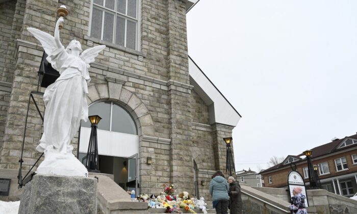 People gather among tributes left on the steps of the church in Amqui., Que., Mar. 14, 2023 in Amqui, Que. (The Canadian Press/Jacques Boissinot)
