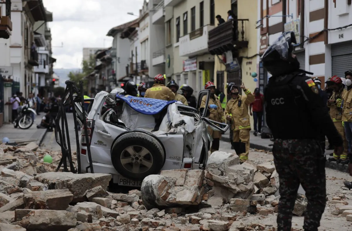 A police officer looks up next to a car crushed by debris after an earthquake shook Cuenca, Ecuador, on March 18, 2023. (Xavier Caivinagua/AP Photo)