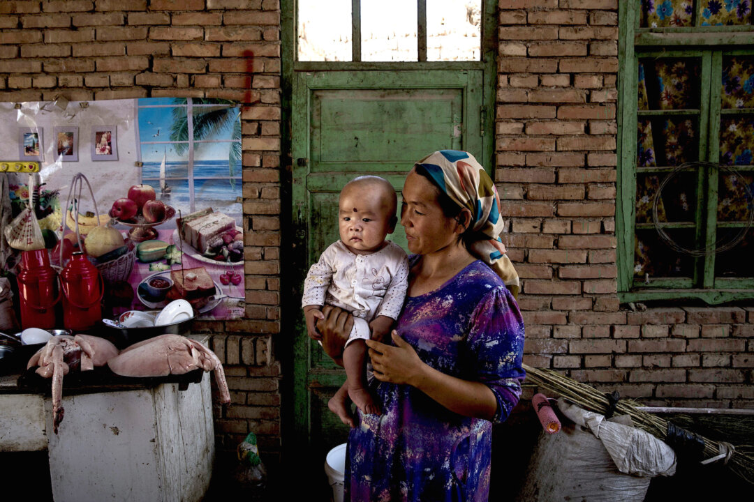 A Uyghur woman holds a child in her home as they prepare food during the Corban Festival in Turpan County, on Sept. 12, 2016. (Kevin Frayer/Getty Images)