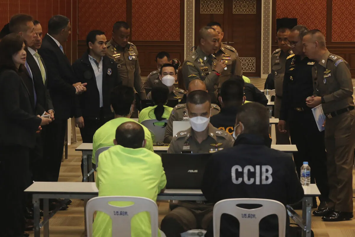 Policemen talk to suspects, wearing light green shirt and sitting back to camera at left side, at Cyber Crime Investigation Bureau in Bangkok, Thailand, on March 22, 2023. (Thailand Cyber Crime Investigation Bureau via AP)