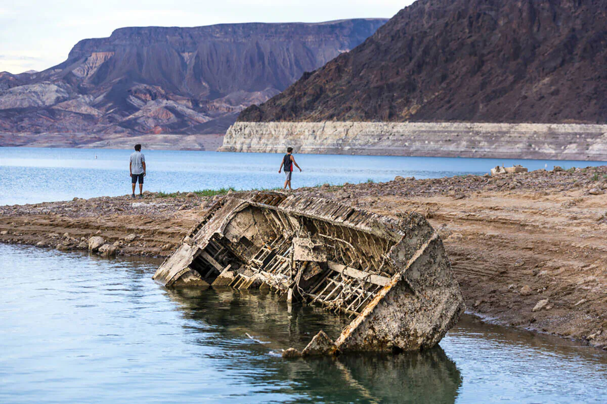 Hikers pass a previously sunken World War II-era Higgins landing craft that once was 185 feet below the surface is nearly on the shoreline as waters keep receding on July 26, 2022, near Boulder City, Nevada. (L.E. Baskow/Las Vegas Review-Journal/TNS)