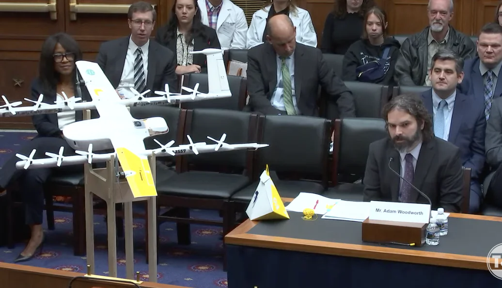 Airplane designer Adam Woodworth (R, at table), CEO of Wing, shows off one of his company's innovative small airplanes at a hearing before a U.S. House of Representatives subcommittee in Washington, on March 30, 2023. (Janice Hisle/The Epoch Times via screenshot of live video.)