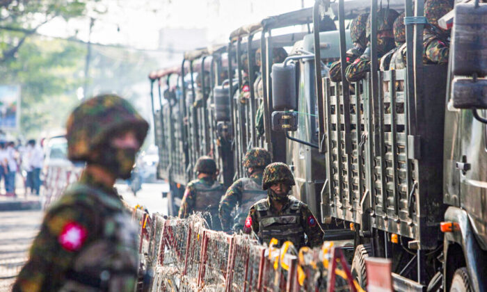 Soldiers stand next to military vehicles as people gather to protest against the military coup, in Yangon, Burma, on Feb. 15, 2021. (Stringer/Reuters)