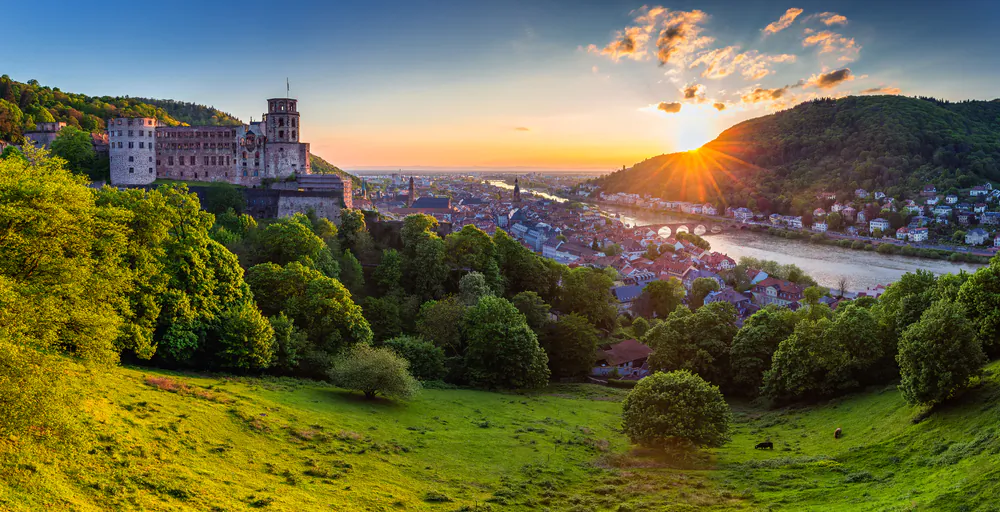 A panoramic view of the town and castle of Heidelberg. The beautiful medieval town and the Neckar River are on the right. On the left, set on a hill 330 feet above the river, is Heidelberg Castle. From its lofty position, the castle has dominated the old town’s skyline for more than eight centuries. (DaLiu/Shutterstock)