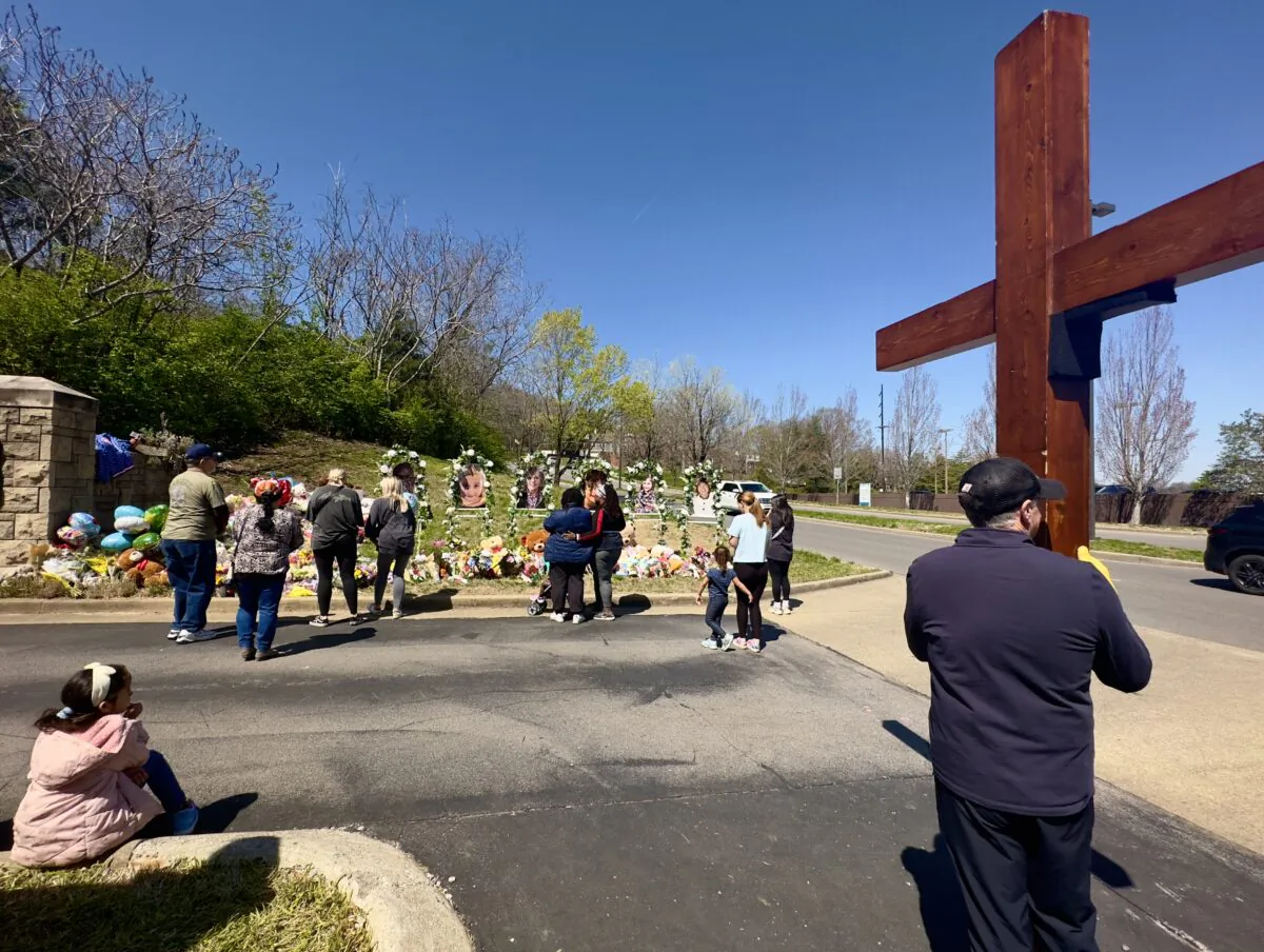 A man holds a large cross in front of The Covenant School in Nashville on Thursday, March 31, four days after six were killed in a mass shooting at the school. Mourners observe the makeshift memorial at the school’s entrance. (Chase Smith/The Epoch Times)