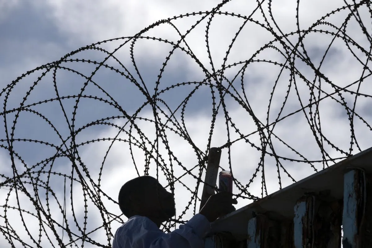 Josue Serrano, a Mexican deported illegal immigrant, hangs wooden crosses on the border fence as part of a vigil for illegal immigrants who died while migrating to the United States, at the U.S.–Mexico border in Playas de Tijuana, Baja California state, Mexico, on July 4, 2022. (Guillermo Arias/AFP via Getty Images)