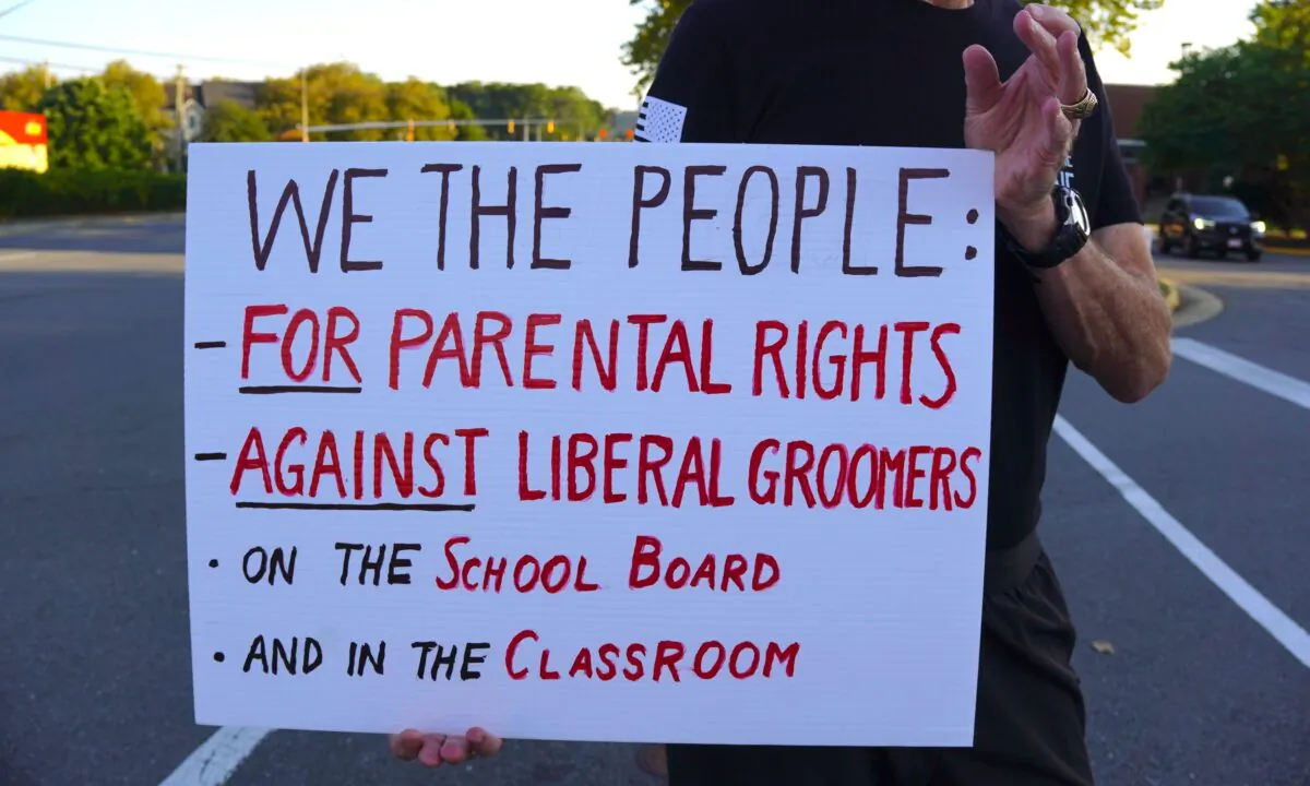 A man holds a sign board at a protest outside Luther Jackson Middle School in Falls Church, Va., before a Fairfax County Public Schools board meeting on Sept. 15, 2022. (Terri Wu/The Epoch Times)