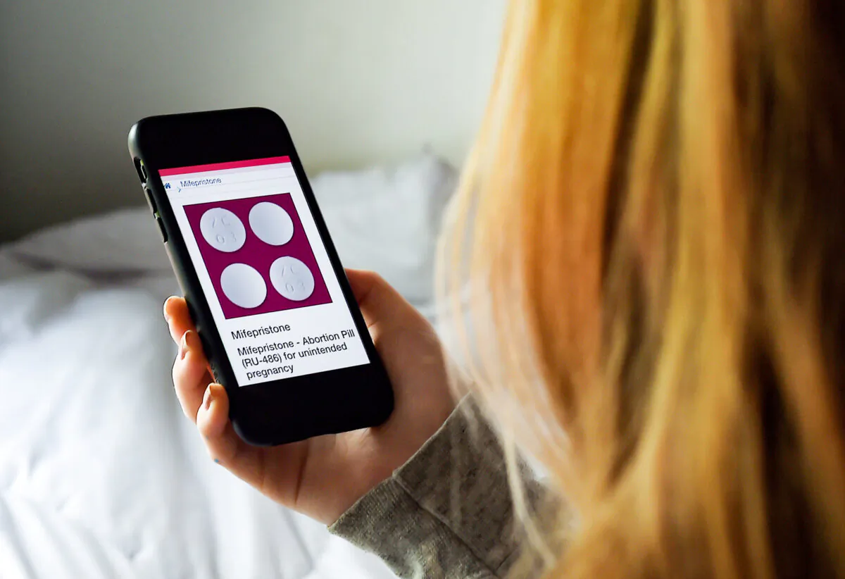 A woman looks at an abortion pill—RU-486, or mifepristone—displayed on a smartphone in Arlington, Va., on May 8, 2020. (Olivier Douliery/AFP via Getty Images)