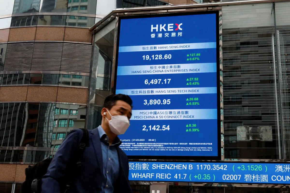 A man walks past a screen displaying the Hang Seng Index at Central district, in Hong Kong, on March 21, 2023. (Tyrone Siu/Reuters)