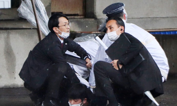 A man (bottom) is detained after throwing an apparent"smoke bomb" in Wakayama, Japan, on April 15, 2023. (STR/JIJI Press/AFP via Getty Images)