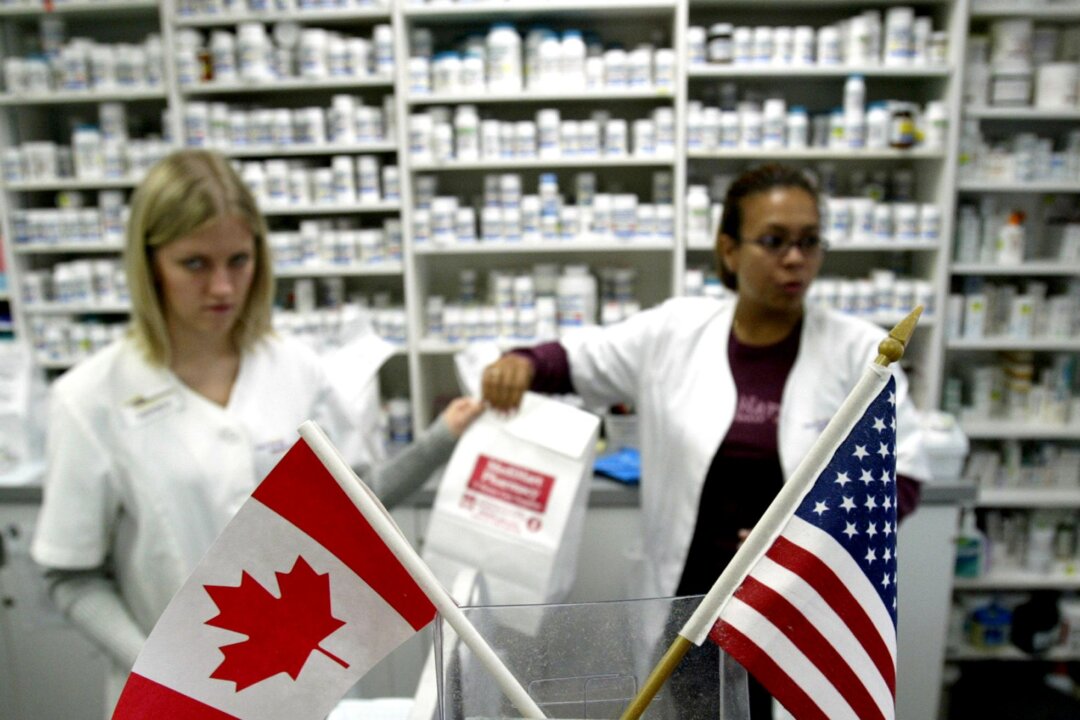 Canadian (L) and American (R) flags sit in the foreground as Canadian pharmacist Amanda Hutchinson (L back) hands fellow pharmacist Florence Ticne (R back) the prescription drugs for a group of Minnesota Senior Citizens from the United States 22 October, 2003 who have traveled nine hours by bus across the US-Canadian border to Winnipeg, Canada to buy cheaper drugs. The Minnesota Senior Federation has set up monthly bus trip to Canada to buy cheaper drugs, with some people saving over 60 percent of the cost of their prescriptions from what they would pay for the same drugs in the United States. AFP PHOTO/Jeff HAYNES (Photo by JEFF HAYNES / AFP) (Photo by JEFF HAYNES/AFP via Getty Images)