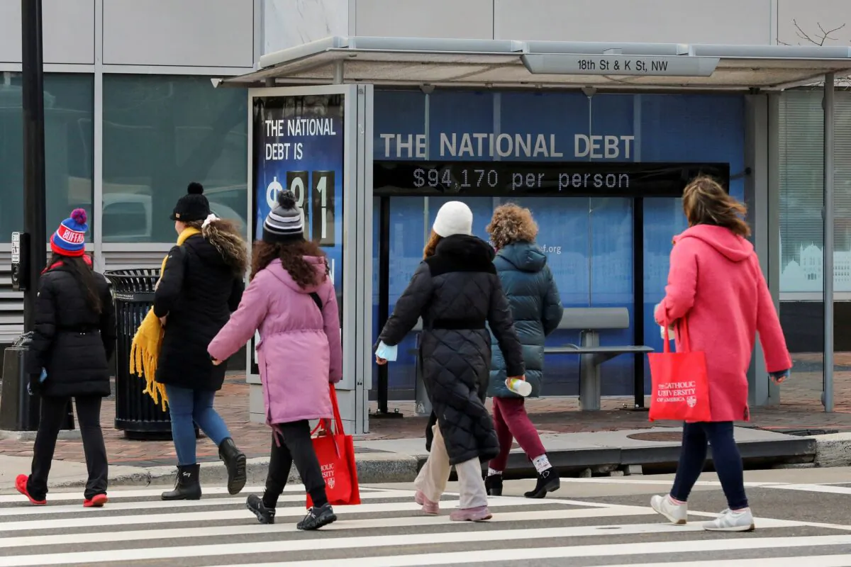 People cross the street next to a bus stop with a sign that shows a U.S. national debt figure in Washington on Jan. 20, 2023. (Amanda Andrade-Rhoades/Reuters)