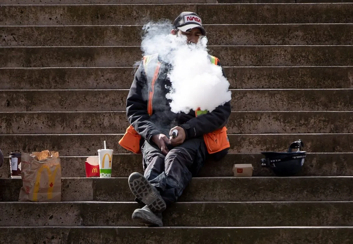 A construction worker exhales after using a vaping device while eating lunch on the steps at Robson Square, in Vancouver, on Mar. 8, 2021. (The Canadian Press/Darryl Dyck)