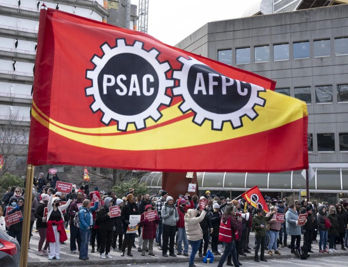 A flag flies as Public Service Alliance of Canada members walk the picket line outside government buildings, April 21, 2023 in Gatineau, Quebec. (The Canadian Press/Adrian Wyld)
