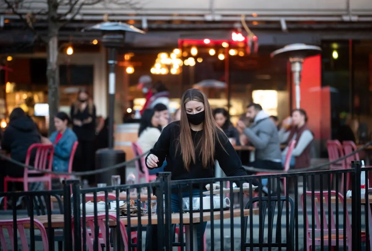 A server clears a table on a patio at a restaurant, in Vancouver, on April 2, 2021. (Darryl Dyck/The Canadian Press)