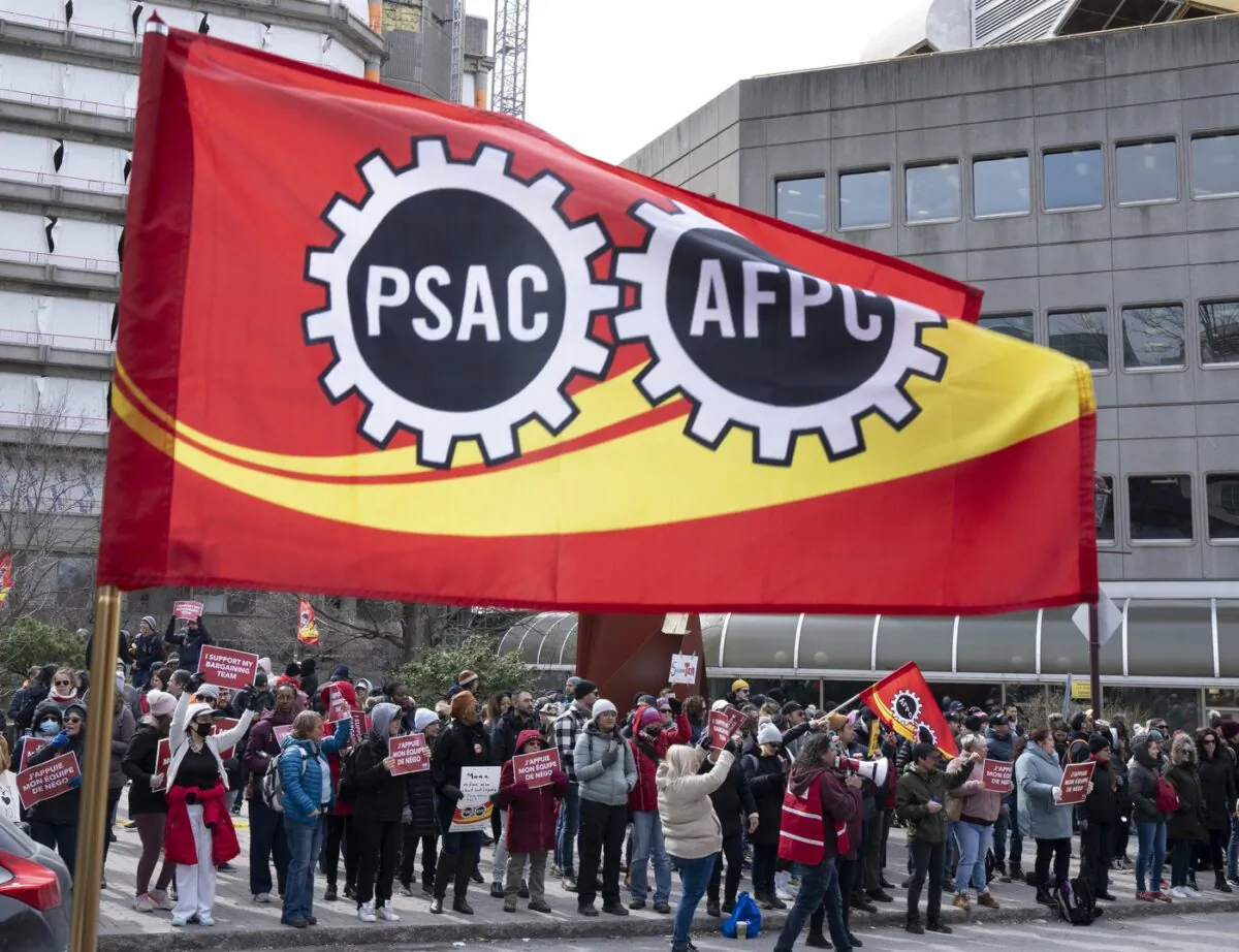 A flag flies as Public Service Alliance of Canada members walk the picket line outside government buildings in Gatineau, Quebec, on April 21, 2023. (Adrian Wyld/The Canadian Press)