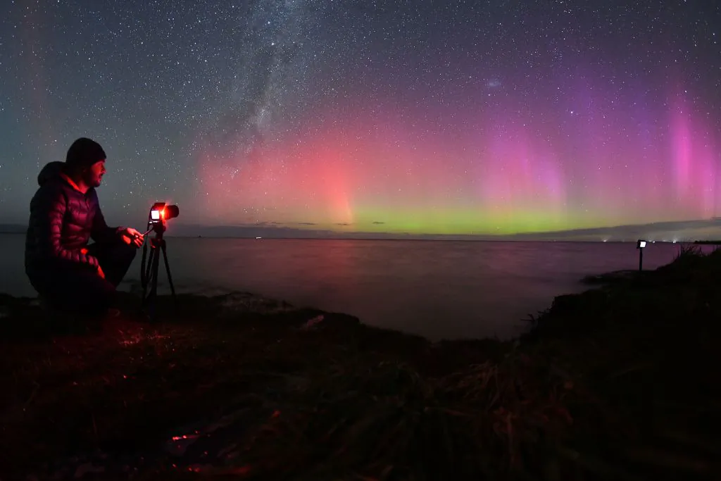 A photographer takes pictures of the Aurora Australis, also known as the Southern Lights, as it glows on the horizon over waters of Lake Ellesmere on the outskirts of Christchurch on April 24, 2023. (Sanka Vidanagama/AFP via Getty Images)