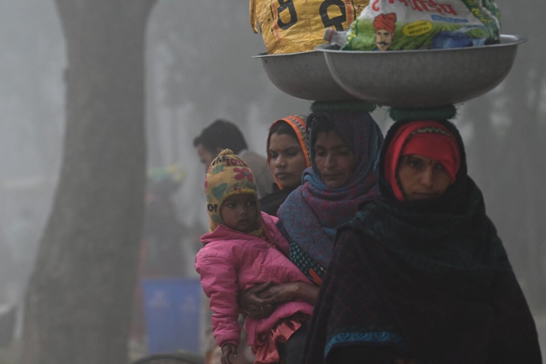 A worker carrying her child walks along a road near India Gate amid heavy smog in New Delhi, on Feb. 22, 2023. ( Arun Sankar/AFP via Getty Images)
