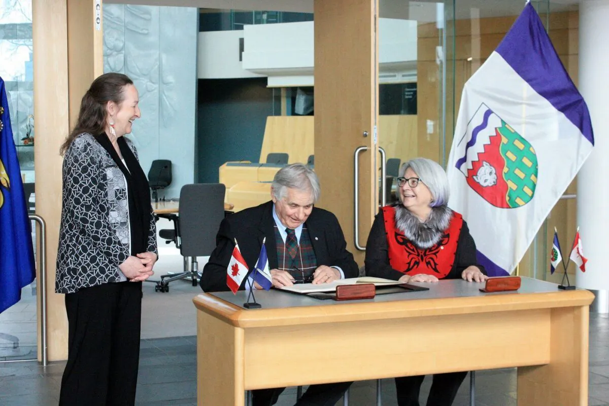 Northwest Territories Premier Caroline Cochrane, left, and Governor General Mary Simon, right, share a laugh as Simon's husband, Whit Fraser, signs the guest book at the Northwest Territories legislative assembly in Yellowknife, April 25, 2023. (The Canadian Press/Emily Blake)