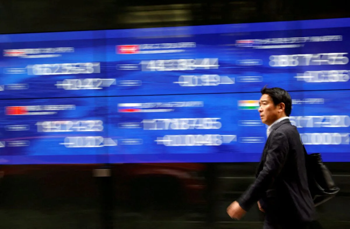 A passerby walks past an electric monitor displaying various countries' stock price index outside a bank in Tokyo, Japan, on March 22, 2023. (Issei Kato/Reuters)