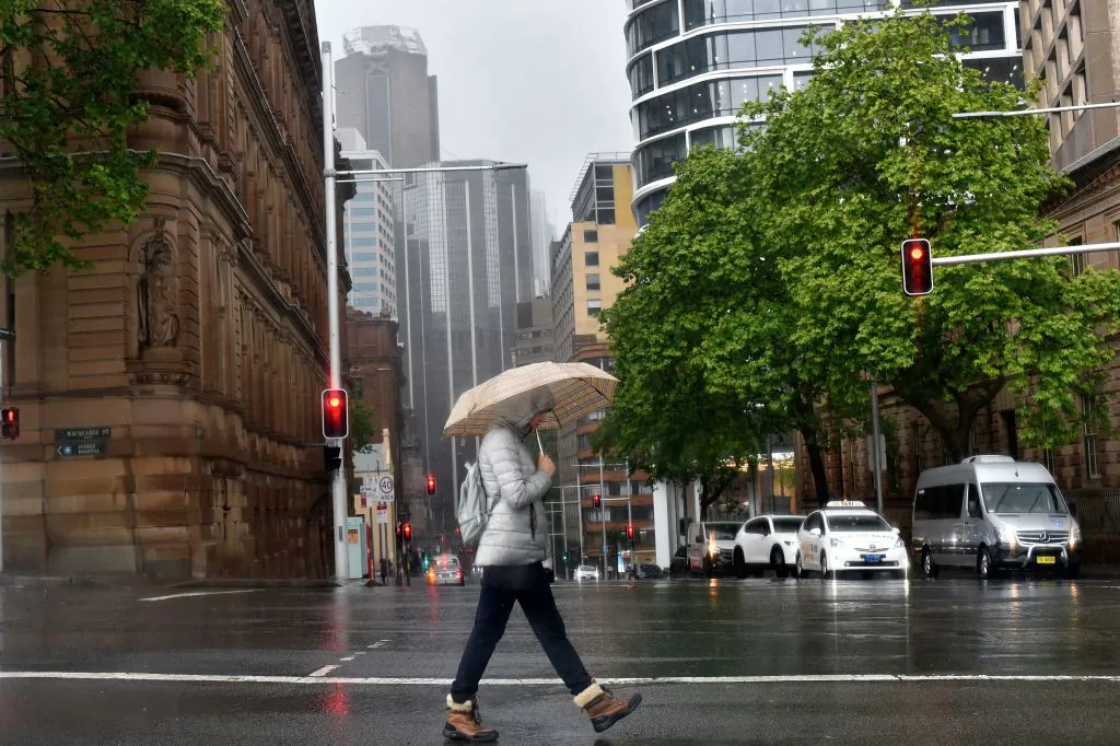 A woman shelters from the rain under an umbrella while crossing a street in Sydney on October 6, 2022. (Photo by Muhammad FAROOQ / AFP) (Photo by MUHAMMAD FAROOQ/AFP via Getty Images)