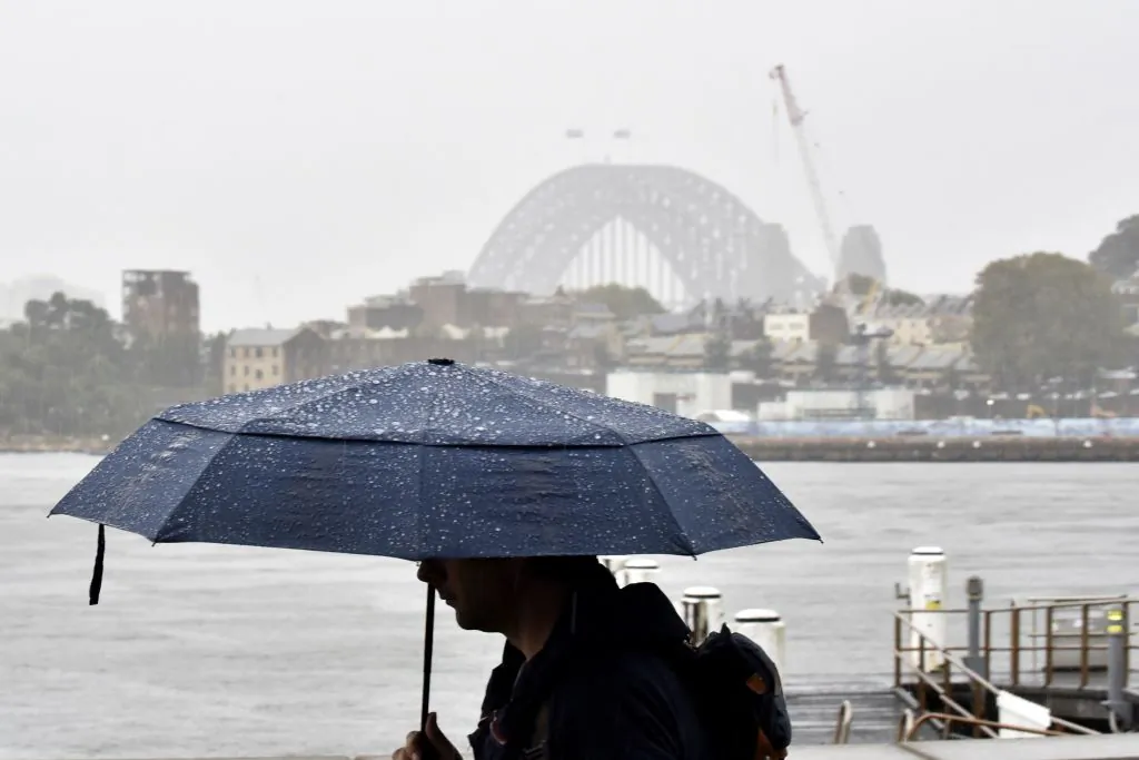 A man walks in front of the Harbour Bridge during rainfall in Sydney on April 7, 2022, as inclement weather triggered evacuation orders in several suburbs of Sydney's south and southwest. (Photo by Muhammad Farooq/AFP via Getty Images)