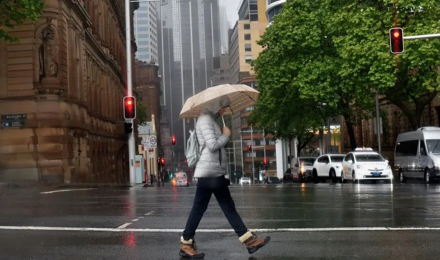 A woman shelters from the rain under an umbrella while crossing a street in Sydney on October 6, 2022. (Muhammad Farooq/AFP via a Getty Images)