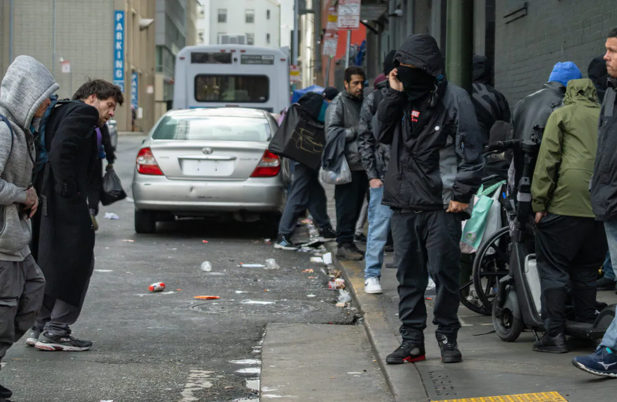 An alleged drug dealer uses his phone near drug users in San Francisco, Calif., on Feb. 22, 2023. (John Fredricks/The Epoch Times)
